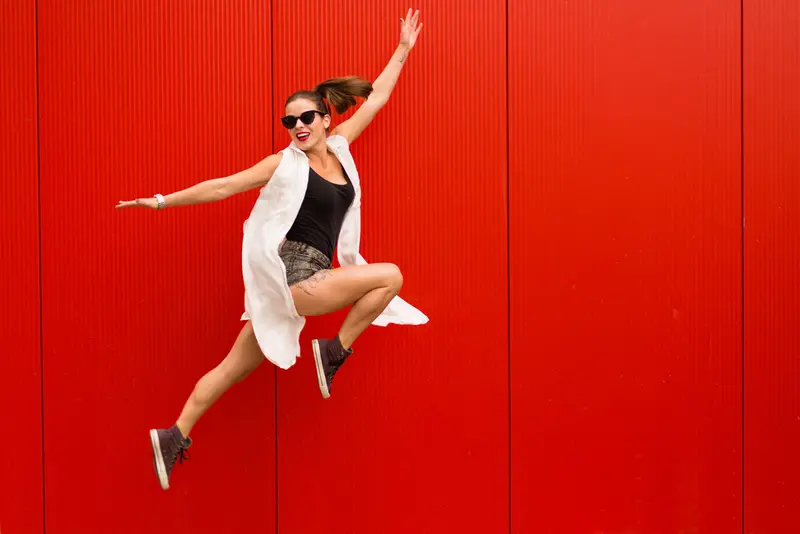 Mujer saltando con alegría frente a una pared roja