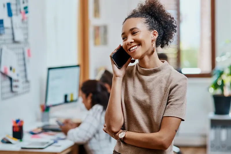 Mujer sonriendo mientras habla por teléfono en la oficina